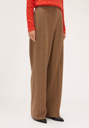 Pantalons à carreaux marron à jambes larges avec une fermeture à bouton et une texture lisse, associés à un pull en tricot torsadé orange vif.