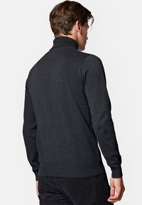 Ciemnoszary sweter dzianinowy z wysokim kołnierzem, prążkowanymi mankietami i dołem. Czysty, dopasowany krój bez wzorów. Wydaje się wykonany z lekkiego materiału.