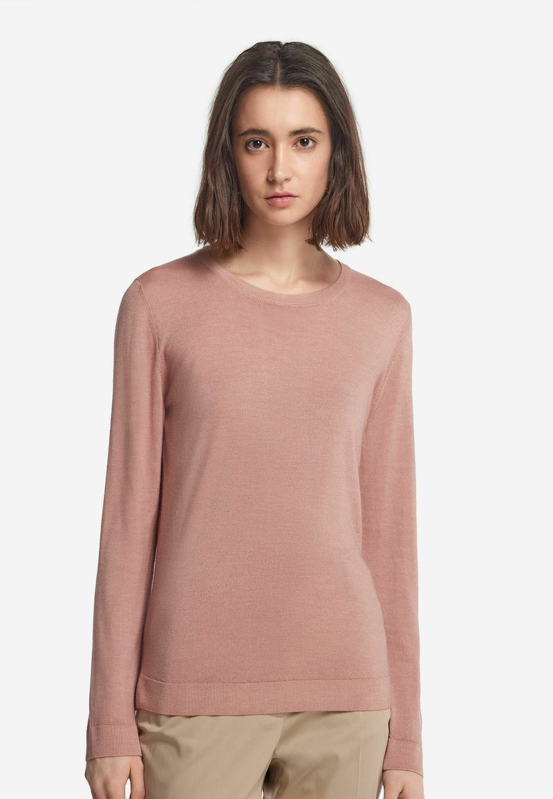 Ljust rosa långärmad tröja i mjukt stickat tyg med rund halsringning och ribbade muddarna och nederkant, i kombination med beige byxor.