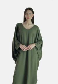Abito oversize verde oliva con scollo a V e maniche a pipistrello pronunciate. Realizzato in un tessuto testurizzato, ha una silhouette fluida. Design minimalista.