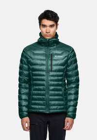 Giacca a vento verde isolata con design a rombi orizzontali, colletto alto, zip frontale e una piccola tasca sul petto con zip.