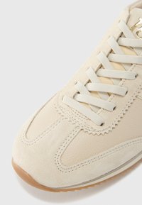 Baskets beige combinant cuir lisse et daim, avec des lacets plats et une semelle en caoutchouc texturée. Soulignées par des détails de surpiqûres discrètes.