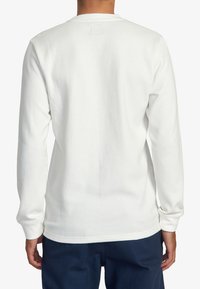 T-shirt à manches longues blanc à rayures, avec un col rond et des manches à poignets, fabriqué en tissu texturé, avec une finition lisse à l'ourlet.