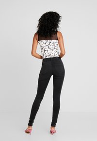 Jeans skinny negros combinados con una blusa blanca y negra de estampado de leopardo que presenta tirantes de malla transparente y un diseño ajustado.