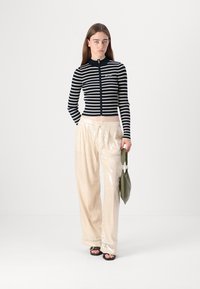 Navy and white striped zip-up cardigan with long sleeves paired with shiny, wide-leg, cream sequin pants, and a green handbag.
