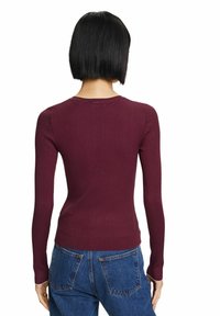 Viininpunainen ribbipintainen pitkähihainen toppi pyöreällä pääntiellä, istuva malli ja teksturoitu kangas. Yhdistetty korkeavyötäröisiin sinisiin farkkuihin.