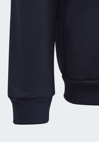 Felpa blu marina con polsini a costine e un tessuto testurizzato. Il design presenta una forma leggermente affusolata con cuciture lisce.