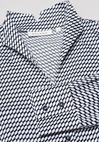 Svart och vit mönstrad skjorta med spetsig krage, diamantformer och knäppte manschettdetaljer. Tyget ser slätt och lätt ut.