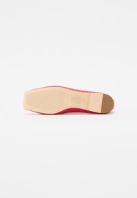 Chaussure plate rouge avec un dessus texturé, un bout en amande et une semelle en caoutchouc beige lisse. Caractéristiques de couture et logo sur la semelle.