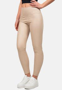 Leggings beige realizzati in un materiale liscio ed elastico con una vita alta, abbinati a sneakers sportive bianche. Design semplice, senza motivi.
