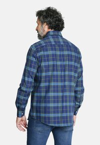Camisa a cuadros azul con acentos en verde y blanco, de manga larga, con cuello abotonado y dobladillo curvado. La tela tiene una textura suave.