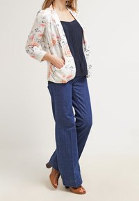 Bloemenprint blazer van lichte stof met lange mouwen en twee zakken, gecombineerd met donkerblauwe wijde jeans en bruine sandalen met hakken.