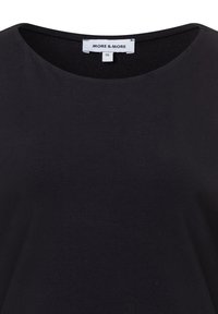 Schwarzes Baumwoll-T-Shirt mit rundem Halsausschnitt und weicher Textur. Das Etikett trägt die Aufschrift "MORE & MORE", Größe 36, in der Nähe des Halsausschnitts platziert.