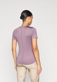 Κοντομάνικη, εφαρμοστή μπλούζα σε απαλό μωβχρώμα ύφασμα, με αόρατο ραφές και λεπτομέρειες ραφής, συνδυασμένη με ανοιχτό μπεζ κολάν.