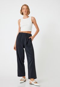 Zwarte wijde broek met een gekreukte textuur, voorzien van een elastische tailleband en zijzakken, gecombineerd met een aansluitend wit geribbeld crop top.