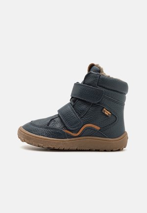 Botte d'hiver enfant en cuir noir avec semelle en caoutchouc marron, deux bandes velcro, doublure en fourrure et détail orange sur le côté.