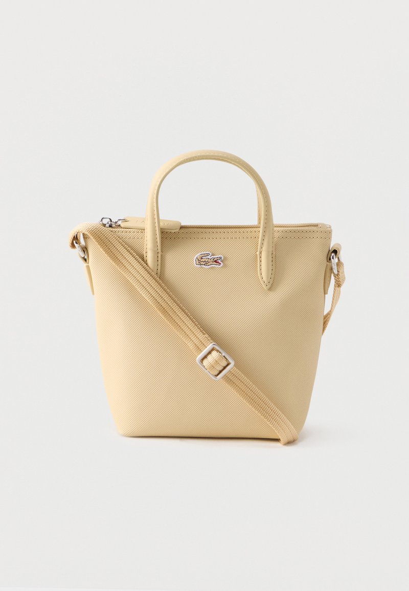 Μπεζ τσαντάκι ώμου με υφή, δύο λαβές, ρυθμιζόμενο λουρί, κλείσιμο με φερμουάρ και μικρό λογότυπο κροκόδειλου στο μπροστινό μέρος.