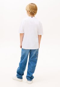 Άσπρο κοντομάνικο μπλουζάκι με λεπτομέρεια στον πίσω γιακά, συνδυασμένο με άνετο μπλε τζιν παντελόνι cargo και λευκά αθλητικά παπούτσια.