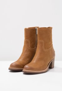 Hnědé kožené kotníkové boty s texturovaným povrchem, které mají boční zip a vrstvený podpatek. Design zahrnuje hladkou špičku a polstrovanou vložku.