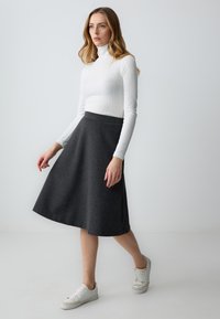 Gonna grigia a campana realizzata in tessuto morbido, abbinata a un dolcevita bianco a coste e sneakers bianche, creando un look casual e coordinato.