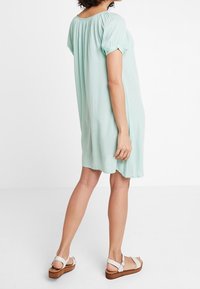 Robe vert menthe clair avec des manches courtes à volants, col froncé et coupe décontractée. Associée à des sandales plate-formes à bout ouvert avec une semelle en bois.