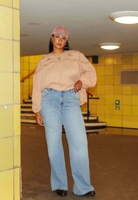 Haut à manches longues rose clair avec broderie florale, associé à un jean évasé taille haute bleu clair et une casquette rose brodée.