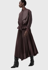 Hnědá kožená bomber bunda s peplum detailem, spárovaná s plisovanou tmavě hnědou sukní a černými koženými vysokými botami.