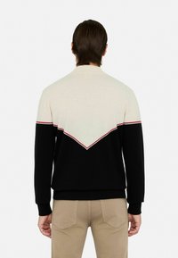 Schwarzer, cremefarbener und roter, farbblockierter Pullover mit einem V-förmigen Design auf dem Rücken, gerippten Bündchen und einem Rundhalsausschnitt.