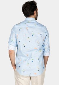 Lichtblauwe shirt met een bloemenpatroon in pasteltinten. De stof is lichtgewicht, en de mouwen zijn opgerold, met een casual achterkant.