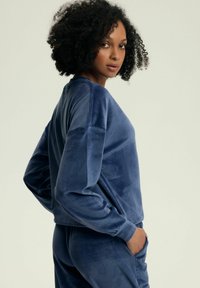 Niebieski welurowy sweatshirt o luźnym kroju, z okrągłym dekoltem i długimi rękawami. Gładka tekstura i subtelny połysk. W komplecie z dopasowanymi spodniami.