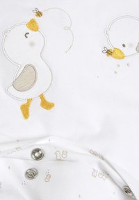 Tissu blanc avec des motifs brodés de canard jaune et d'abeille. Détail de fermeture à pression en bas avec de petits motifs de canard dans des couleurs claires.