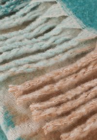 Texturovaný šátek s jemnými, sm�íšenými odstíny tyrkysové a béžové, se třásněmi na koncích. Vyrobeno z lehkého, chlupatého materiálu.