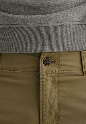 Vyötäröalue, jossa näkyy harmaa ribbineulosneulos neuleen helmasta khakinväristen, napitettujen housujen yläpuolella, joissa näkyy ompeleet ja brändätty nappi.