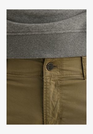 Taillenbereich mit grauem, geripptem Saum eines Pullovers über khakifarbenen, geknöpften Hosen mit sichtbarer Naht und einem markierten Knopf.