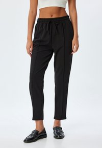 Schwarze, taillierte Jogginghose mit einem elastischen Bund und Kordelzug, ausgestattet mit seitlichen Nahtdetails und einer glatten, weichen Textur.