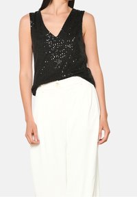 Svart paljettärmad topp med v-ringning, i kombination med vita högmidjade byxor som har en avslappnad passform och texturerad tyg.