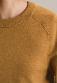 Brązowy sweter dzianinowy z prążkowanym okrągłym dekoltem i teksturowaną powierzchnią, z raglanowymi rękawami i miękkim, oddychającym materiałem.