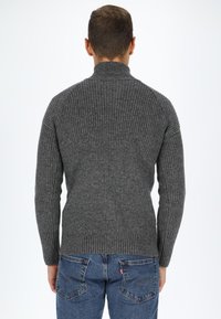 Maglione grigio a coste con un colletto alto, caratterizzato da un design aderente e maniche lunghe, abbinato a jeans blu.