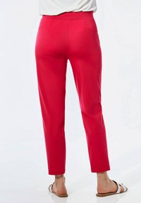 Rote, taillierte Hosen mit glatter Textur, schmal zulaufenden Beinen und Gesäßtaschen, kombiniert mit hellbraunen Sandalen mit dünnem Riemen.