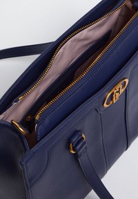 Borsa a tracolla in pelle blu navy con un design strutturato, zip dorate e un'accento in hardware dorato. L'interno presenta una fodera rosa chiaro e scomparti.