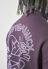 Lila Sweatshirt mit hohem Kragen, ausgestattet mit weißen grafischen Illustrationen und Text auf der Rückseite. Weicher, strukturierten Stoff.