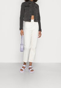 Chaqueta corta de mezclilla negra, pantalones blancos de talle alto, bolso de hombro lila y sandalias lila a juego con correas que dicen "BUFFALO".