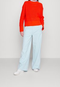 Jasnopomarańczowy sweter z żebrowanym wykończeniem, luźny krój. Jasnoniebieskie spodnie o szerokich nogawkach, gładki materiał, w połączeniu z białymi sneakersami. Prosty styl, bez wzorów.