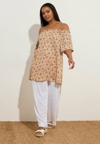 Top floreale off-the-shoulder nei toni dell'arancio e del giallo, in tessuto leggero, abbinato a pantaloni bianchi larghi e sandali in espadrille beige.