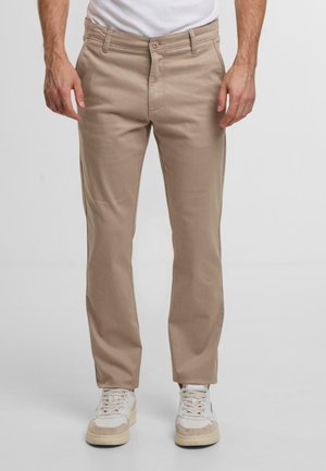 Beige Baumwollhose mit geradem Bein, mit Knopfverschluss, Gürtelschlaufen und Seitentaschen, getragen mit weißen Sneakers.