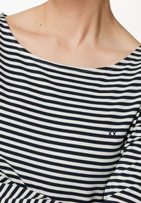 Svart-vit randig topp tillverkad av ett mjukt material; har en bred nacke och lätt ärmdetalj; diskret broderad logotyp nära fållen.