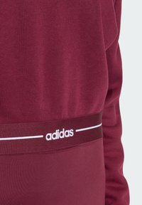 Bordowa bluza z miękką fakturą, elastycznym pasem z białym logo Adidas oraz prostym, czystym designem.