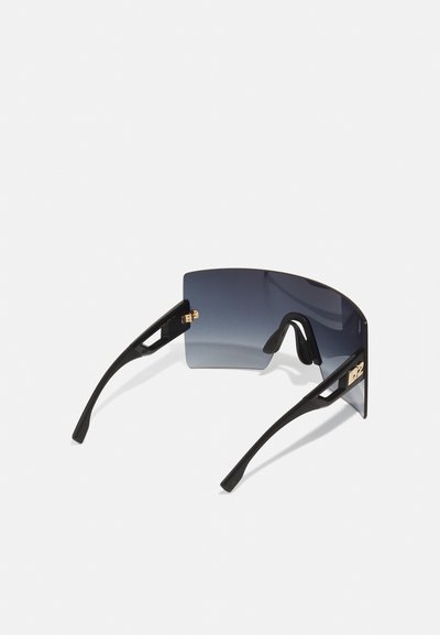 Óculos de sol oversized pretos com formato retangular, lentes cinza com gradiente e detalhes em ouro nas hastes. Acabamento com textura mate.