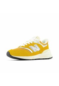 Gul sportssko med mocka och mesh-material, med en vit logotyp, kontrasterande sömmar och en svart gummisul.