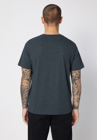 Tmavě šedé tričko s krátkými rukávy, kulatým výstřihem, vyrobené z měkké látky. Má hladkou texturu a volný střih. Jednoduchý, zdobením nezasahující design.